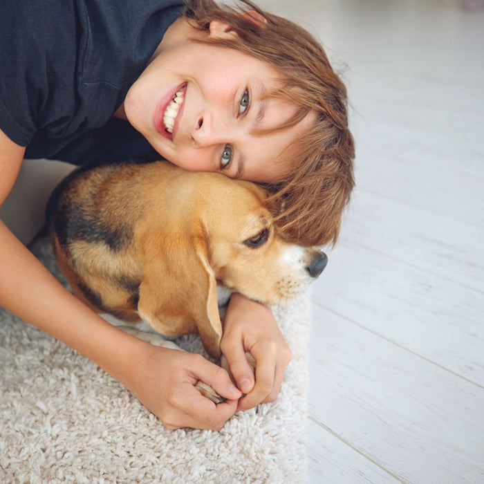 A smiling child hanging off the side of the couch hugging the pet dog